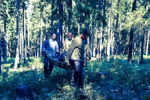 Drei Personen tragen eine improvisierte Trage durch einen Wald