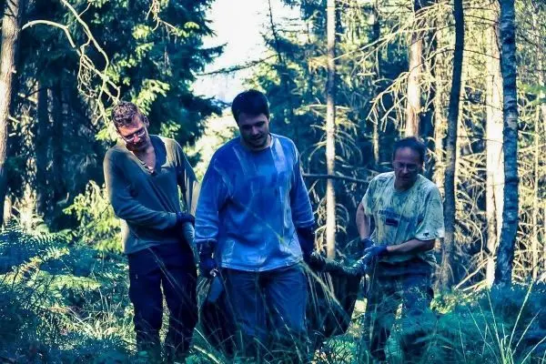 Drei Personen tragen eine schwere Last durch einen Wald