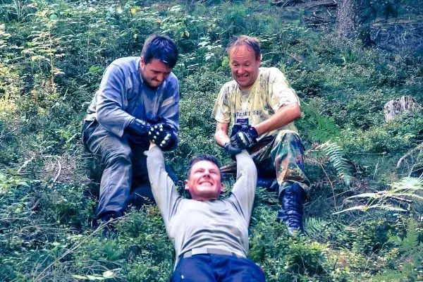 Drei Personen ziehen einen Mann über den Boden in einem bewaldeten Gebiet