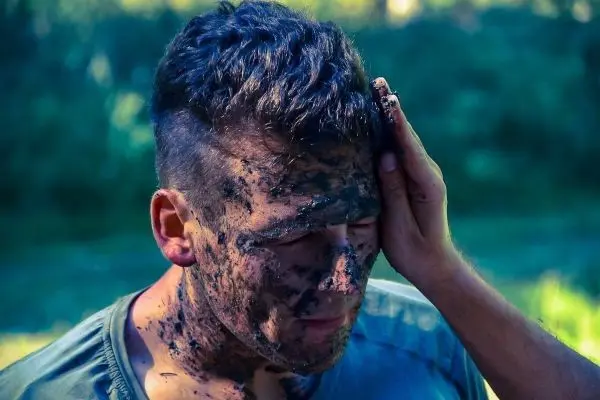 Hände verteilen Schlamm auf dem Gesicht einer Person im Freien