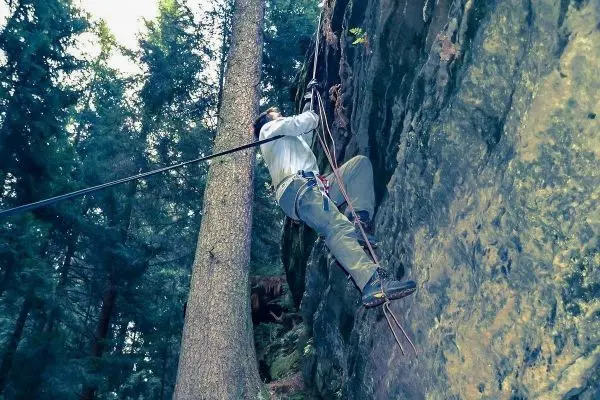 Kletterer sichert sich mit Seil an einer Felswand im Wald