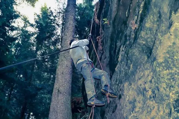 Kletterer sichert sich mit Seil an einer Felswand und einem Baum
