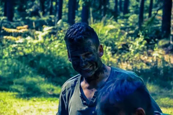 Lächelnder Teilnehmer mit Gesichtsschminke aus Erde in bewaldeter Umgebung