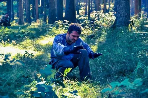 Mann kniet im Wald und untersucht den Boden mit beiden Händen