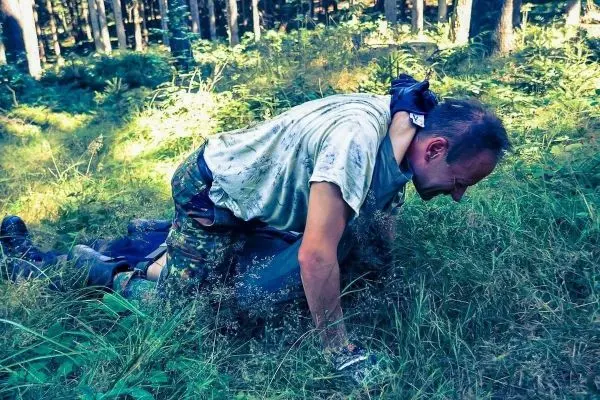 Mann kriecht durch hohes Gras im Wald
