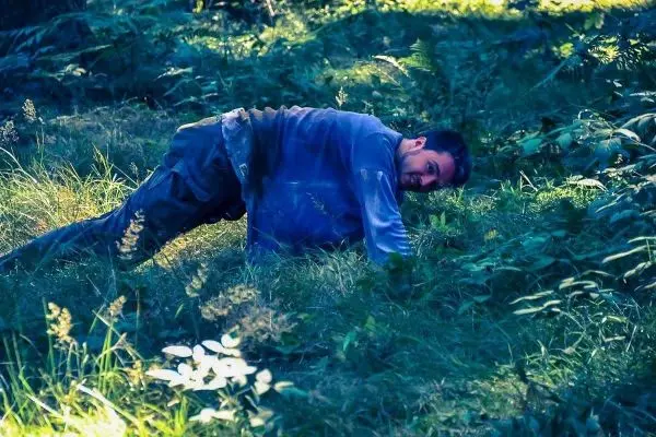 Mann kriecht durch hohes Gras in einem Waldgebiet