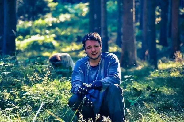 Mann sitzt im Wald auf dem Boden zwischen Pflanzen und Bäumen