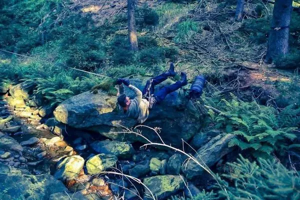 Mann überquert mit Seil eine Felsformation in einem bewaldeten Gebiet