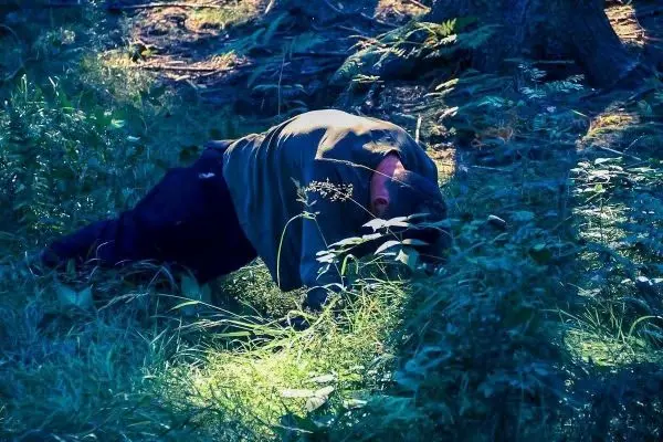 Person in der Bauchlage auf dem Boden zwischen hohem Gras und Pflanzen