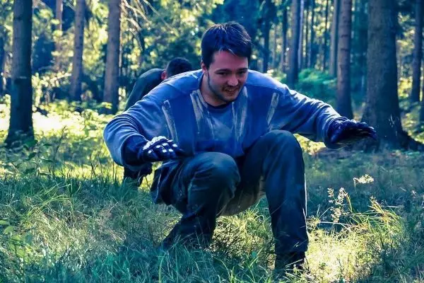 Person in Hockehaltung im Gras, umgeben von Bäumen und Pflanzen