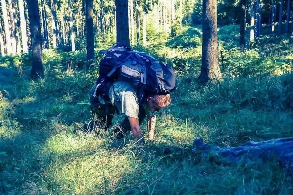 Person krabbelt durch hohes Gras im Wald mit einem großen Rucksack