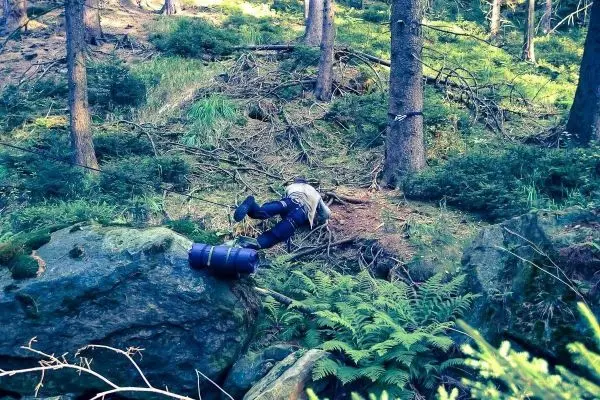 Person liegt auf dem Boden neben einem großen Stein im Wald