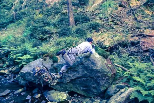 Person überquert großen Felsen in einem bewaldeten Gebiet