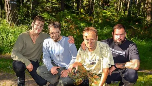 Vier Personen posieren im Wald mit camouflierter Gesichtsbemalung