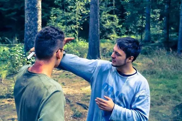 Zwei Personen im Wald, einer zeigt auf eine Verletzung am Arm des anderen