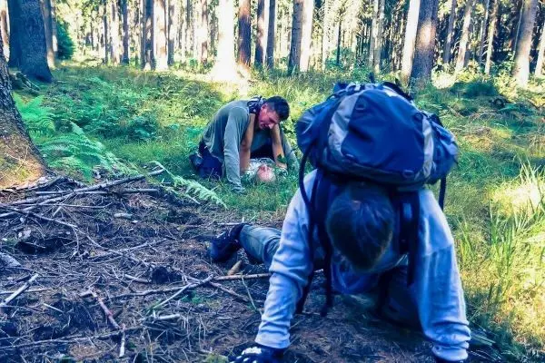 Zwei Personen in einem Wald, eine kniet auf dem Boden und hilft der anderen