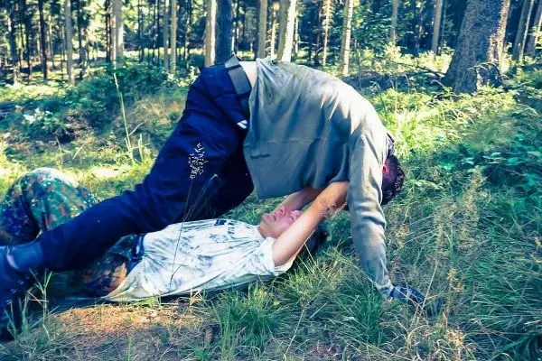 Zwei Personen liegen im Gras, eine Person drückt die andere nach unten