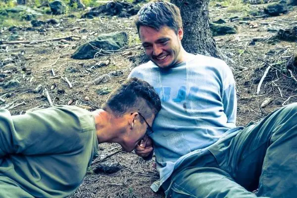 Zwei Personen sitzen auf dem Boden im Wald und lachen miteinander
