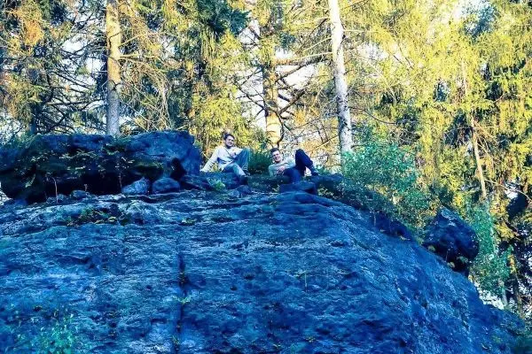 Zwei Personen sitzen auf einem großen Felsen umgeben von Bäumen