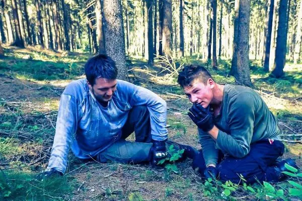 Zwei Personen sitzen im Wald auf dem Boden und betrachten Pflanzen