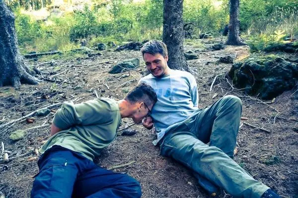 Zwei Personen sitzen im Wald auf dem Boden und interagieren miteinander