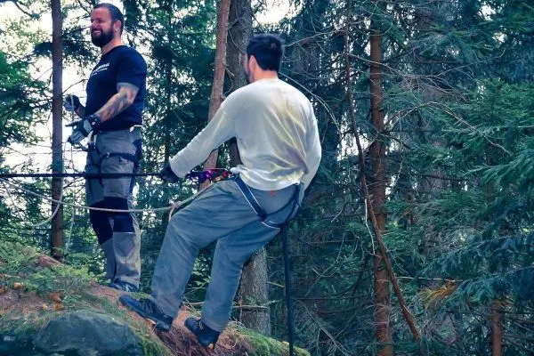 Zwei Personen stehen an einer selbstgebauten Seilquerung zwischen Bäumen