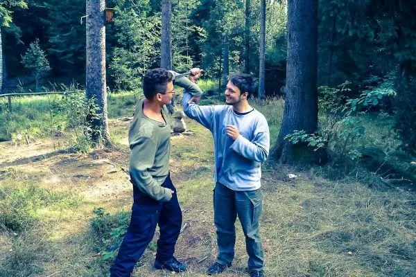 Zwei Personen stehen in einem Wald und üben eine Kampfsituation