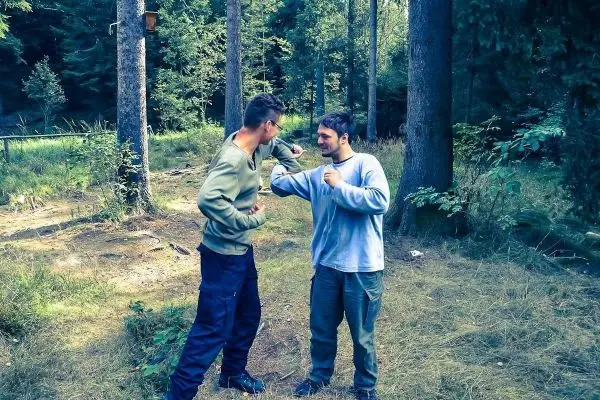 Zwei Personen üben eine Kampfsituation im Wald, stehen sich gegenüber
