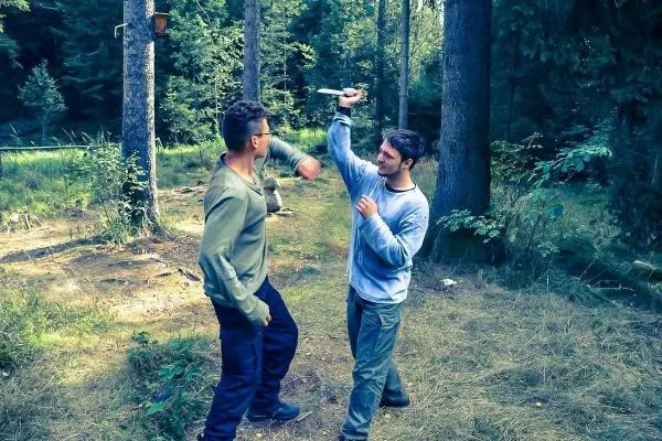 Zwei Personen üben eine Selbstverteidigungstechnik im Wald mit einem Messer
