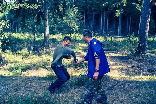 Zwei Personen üben eine Technik zur Handentwaffnung im Wald