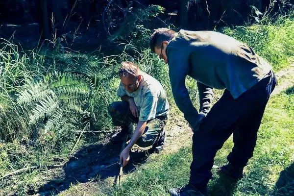 Zwei Personen untersuchen den Boden am Rand eines kleinen Baches