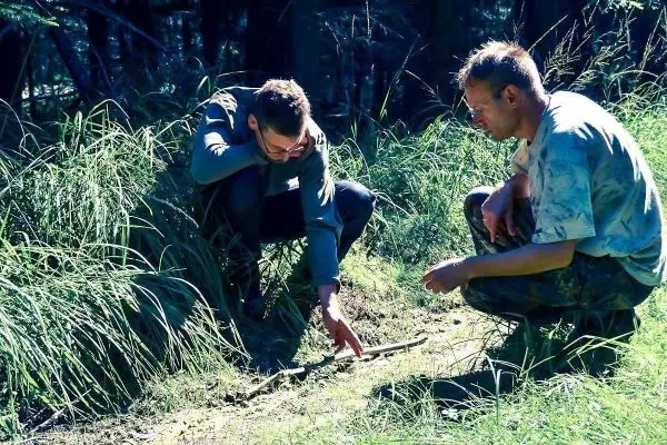 Zwei Personen untersuchen den Boden im Gras und zeigen auf einen Stock
