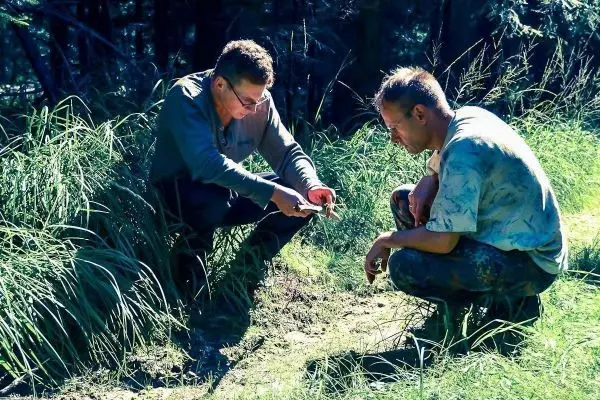 Zwei Personen untersuchen den Boden und halten ein Messer in der Hand