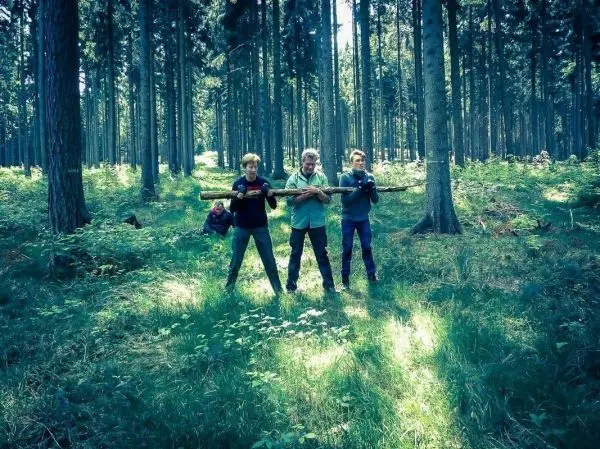 Drei Personen halten einen langen Stock in einem Waldgebiet