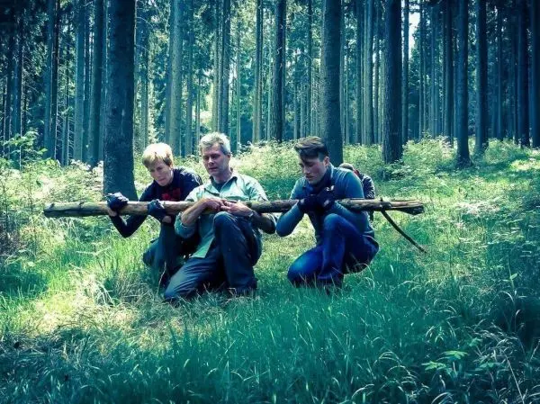 Drei Personen halten gemeinsam einen langen Stock im Wald