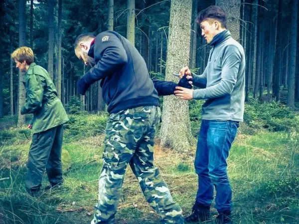 Drei Personen im Wald üben eine Technik zur Unterstützung oder Rettung