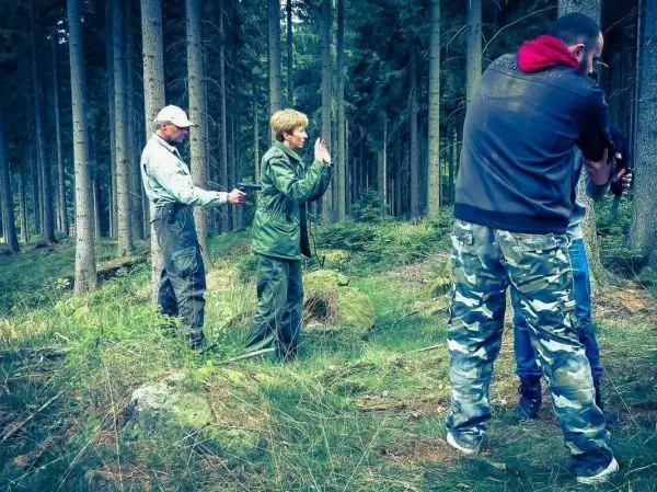 Drei Personen in einem Wald, eine Person zeigt eine Abwehrhaltung