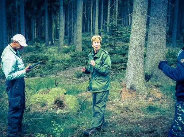 Drei Personen stehen im Wald und betrachten ein Gerät sowie eine Pflanze