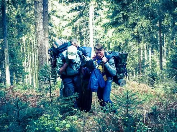 Drei Personen tragen große Rucksäcke und bewegen sich durch einen Wald