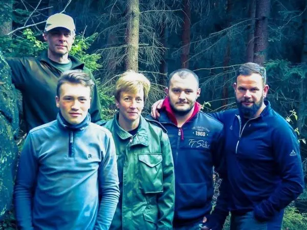Fünf Personen stehen in einem Wald zwischen Bäumen und Sträuchern