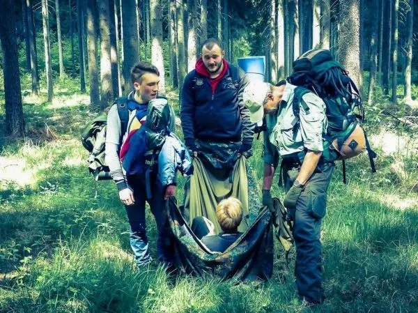Gruppe von Personen um eine liegende Person in einer Trage im Wald beim Überlebenstraining