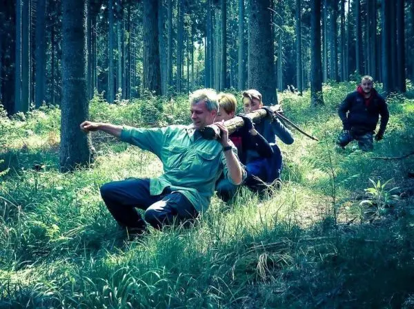 Gruppierung von Personen im Wald, eine Person trägt einen Stock über der Schulter