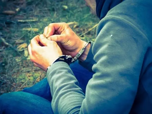 Hände fädeln einen Draht durch eine Schlaufe, Handfesseln sichtbar