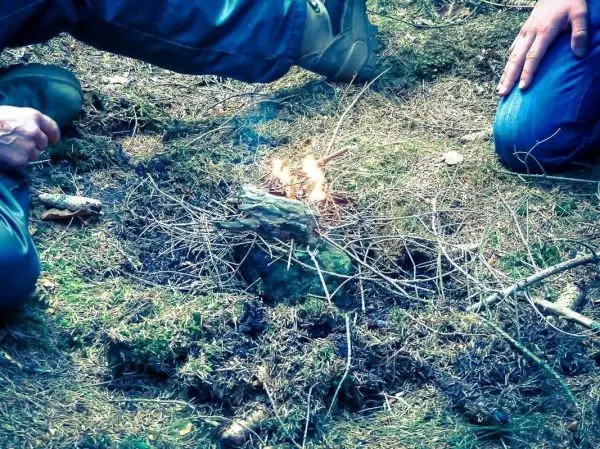 Hände halten Zweige über einem kleinen Feuer im Wald