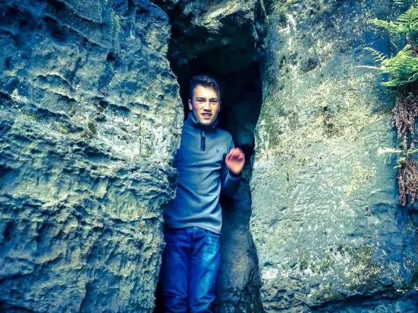 Junge steht in einer Felsspalte zwischen grauen Felsen und grüner Vegetation