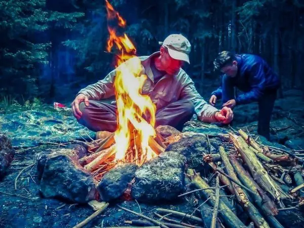 Kleine Flamme brennt zwischen Steinen, während eine Person Zunder vorbereitet