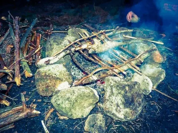 Kleines Bodenfeuer mit Steinen umgeben, Rauch steigt auf