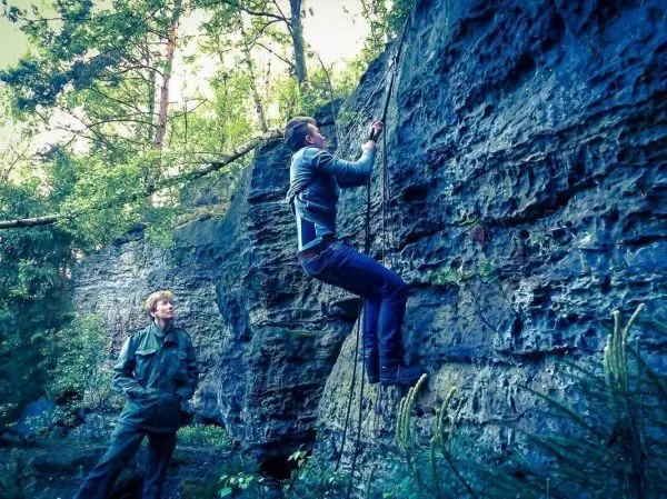 Kletterer nutzt Seil, um eine Felswand zu erklimmen, während ein Beobachter zusieht