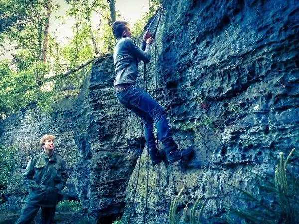 Kletterer nutzt Seil zur Besteigung einer Felswand, Beobachter steht daneben