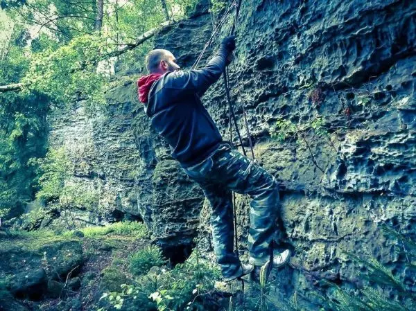 Kletterer nutzt Seil zur Besteigung einer Felswand im Wald